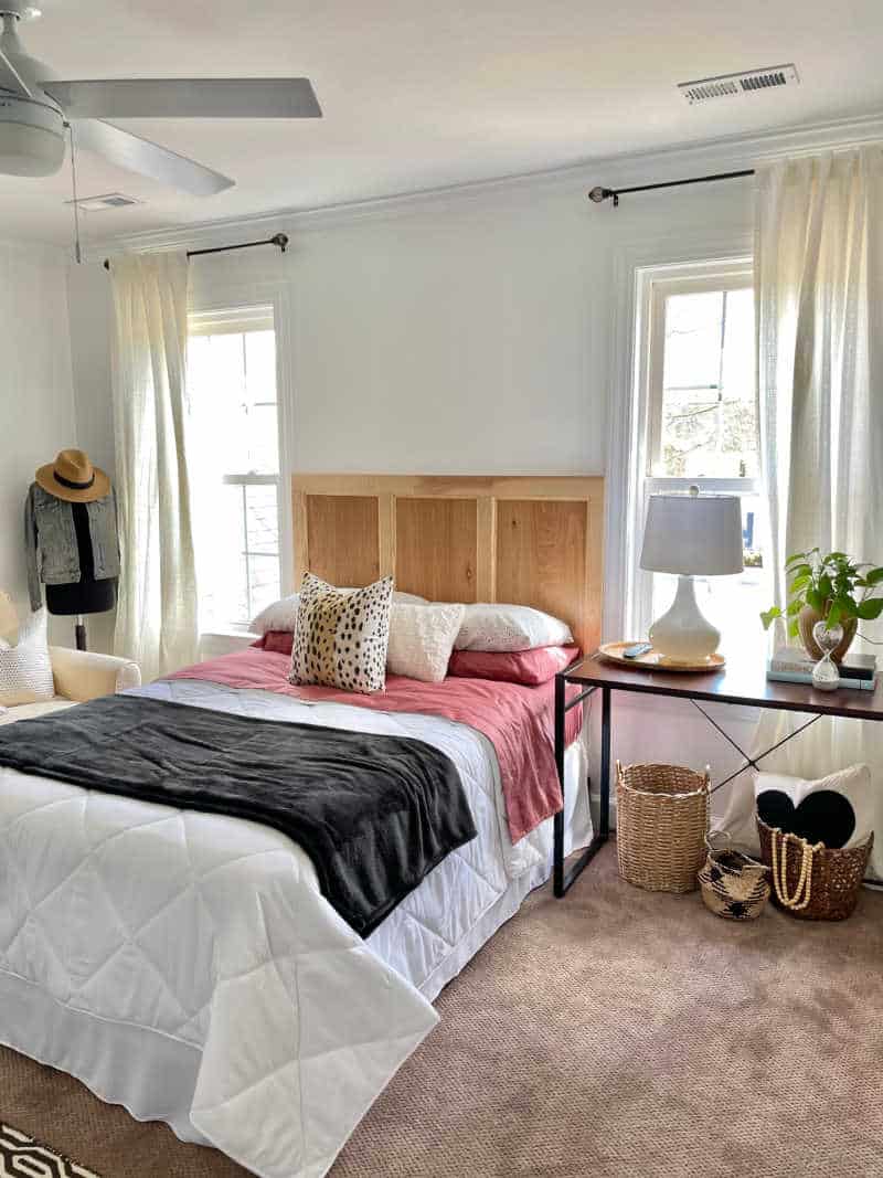 bed with white comforter next to a desk night stand and baskets