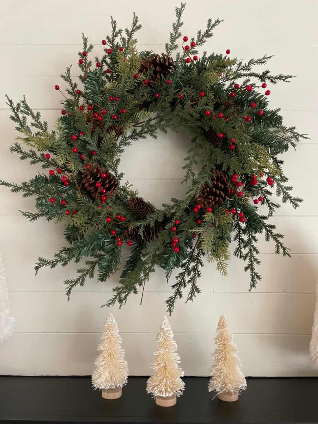 Artificial wreath with pinecones and red berries added hanging on mantle