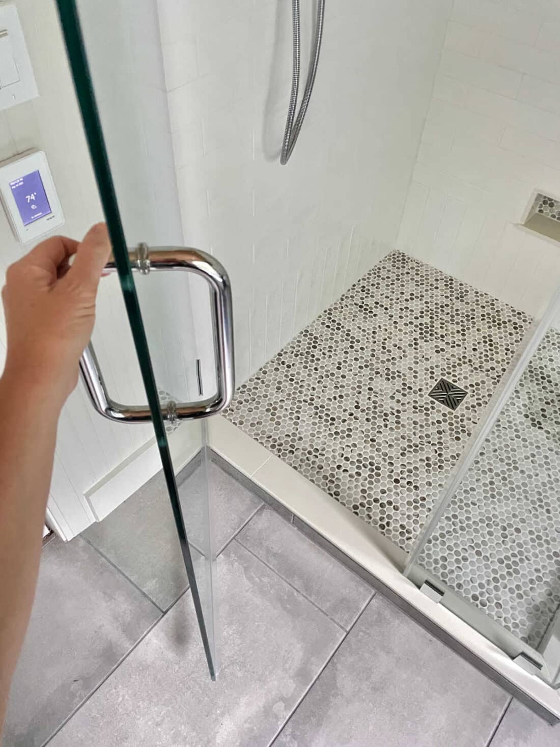 Shower door open to see penny tile on floor